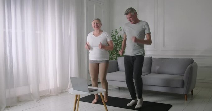 Happy senior couple enjoying physical activity at home, running in place together. Lazy husband making funny absurd gestures.