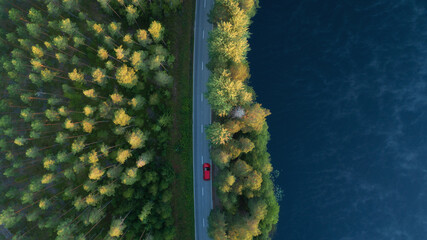 Aerial view of lake, forest and road at misty morning. Red car driving through the forest at sunrise. Highway through deep forest.
