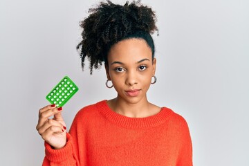 Young african american girl holding birth control pills thinking attitude and sober expression looking self confident