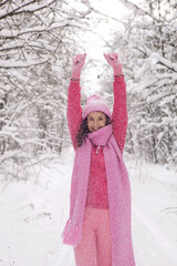 Obraz premium woman in pink clothes a jacket a knitted scarf and a hat stands in a snowy forest in winter