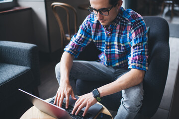Crop focused student doing homework on laptop in cafeteria