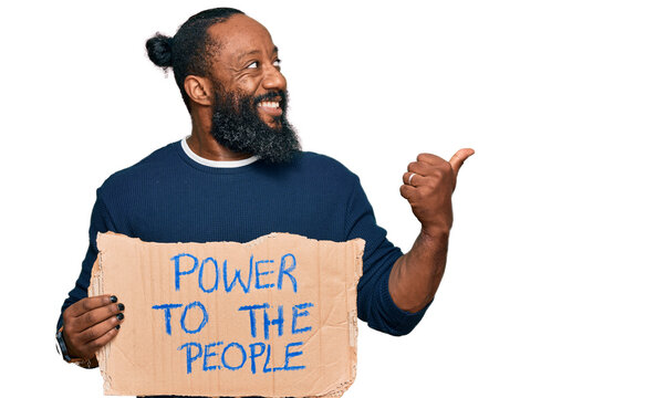 Young african american man holding power to the people banner pointing thumb up to the side smiling happy with open mouth