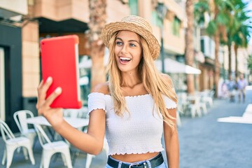 Young blonde tourist girl smiling happy doing video call using touchpad at the city.