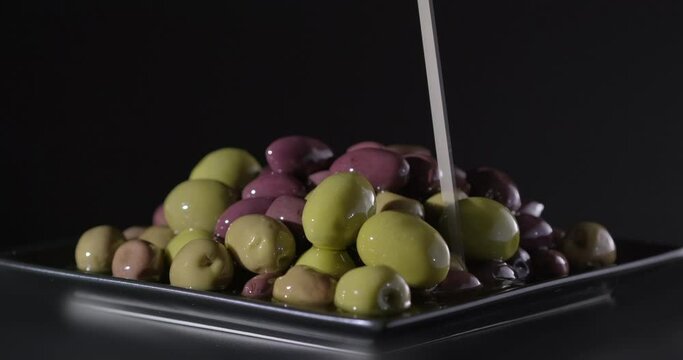 Olives. Shot of Pouring Fresh Olive Oil on Olives, rotation on black background, slow motion, close up, macro. Mediterranean fresh healthy food ingredient