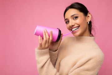 Naklejka premium Beautiful young positive brunette woman wearing casual stylish clothes isolated over colorful background wall holding paper cup for mockup drinking coffee looking at camera