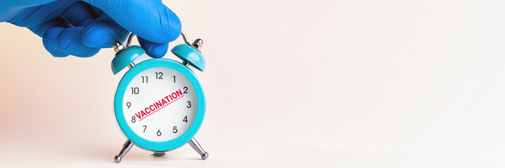 medical person holding alarm clock over grey background. copy space. studio shot. minimal....