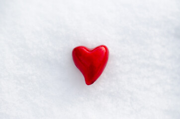 A red heart lies in the snow. Valentine's day background with place for text