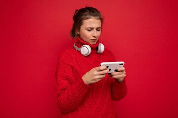 Attractive upset young brunet woman wearing red sweater isolated over red background wall holding...