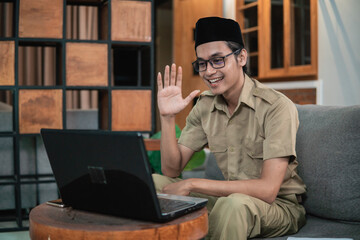 man in civilian uniform use laptop while sitting with hand gestures to say hello when working online at home