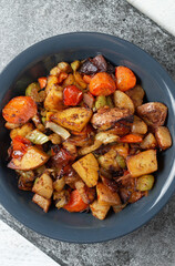 Stewed vegetables with spices in a dark blue plate on a dark gray slate or stone background. View from above.
