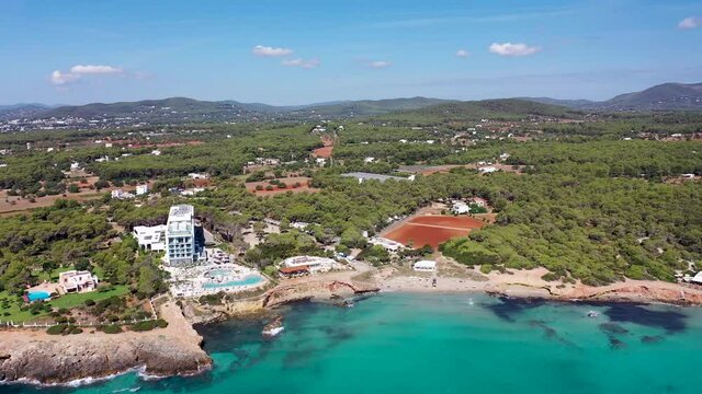Aerial footage of the beautiful island of Ibiza, Spain in the Balearic islands showing the beach and hotels by the mediterranean sea in the village of Playa Es Canar and the scenic mountains behind