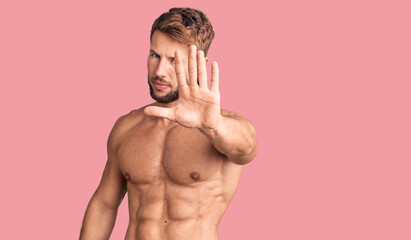 Fototapeta premium Young caucasian man standing shirtless doing stop sing with palm of the hand. warning expression with negative and serious gesture on the face.