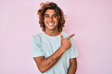 Young hispanic man wearing casual clothes cheerful with a smile of face pointing with hand and finger up to the side with happy and natural expression on face