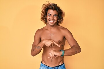 Young hispanic man standing shirtless in hurry pointing to watch time, impatience, upset and angry...