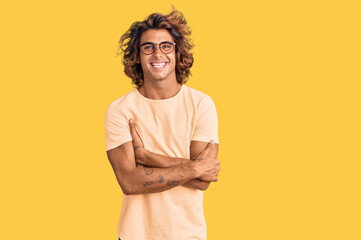 Young hispanic man wearing casual clothes and glasses happy face smiling with crossed arms looking...
