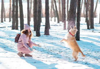 Happy beautiful young woman blowing snowflakes from her hands to her dog golden retriever in a winter day. Friendship, pet and human.