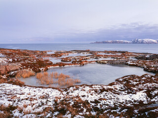Wonderful mountain landscape with a cape on the shore of the Barents sea. Amazing sunrise landscape with polar white snowy range of mountains.