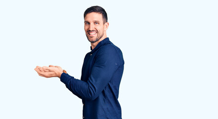 Young handsome man wearing casual shirt pointing aside with hands open palms showing copy space, presenting advertisement smiling excited happy
