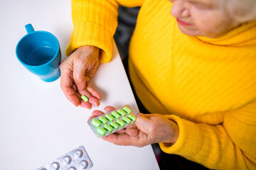 Obraz premium Ill old woman taking a pill from a pill dispenser in her house