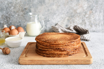 Fototapeta na wymiar stack of thin pancakes on a wooden board. Pancake ingredients: flour, milk, eggs, whisk on the kitchen table.