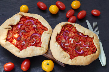 Tomato tarts with onion rings on the wooden board decorated with various cherry tomatoes. Traditional Italian vegetarian food on the black background