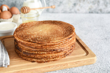 stack of thin pancakes on a wooden board. Pancake ingredients: flour, milk, eggs, whisk on the kitchen table.