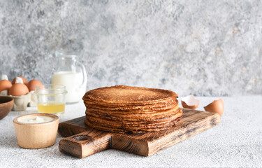 Fototapeta na wymiar stack of thin pancakes on a wooden board. Pancake ingredients: flour, milk, eggs, whisk on the kitchen table.