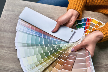Color wheel for choosing paint tone. Hands of female interior designer working with palette for choosing colors. Creative process concept. Comparing options with matching hues.