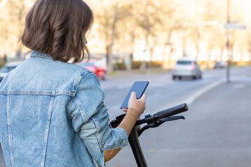 Studentin in Jeans Jacke bezahlt mit Smartphone für E Scooter