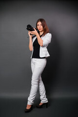 A woman in a white suit with a camera in her hands posing while standing on a black background. Contemporary photographer in the studio.