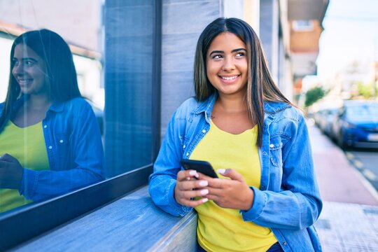Young latin woman smiling happy using smartphone at the city.