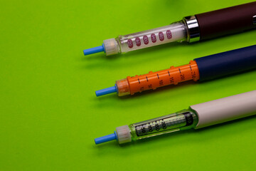 Three insulin injector for diabetes therapy, on a green background. Close-up. Plastic insulin injector. 