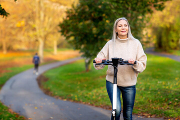 Grauhaarige Weißhaarige Frau fährt E Scooter in Park in Helm