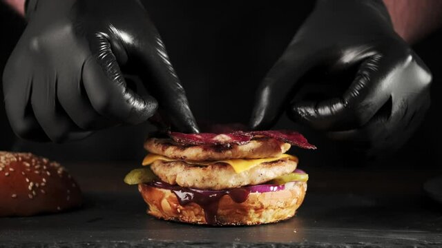 Making burger close-up, the hand of a chef in black gloves prepares a burger or cheeseburger with a double cutlet on a slate board.