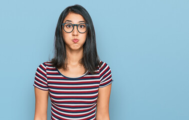 Beautiful asian young woman wearing casual clothes and glasses puffing cheeks with funny face. mouth inflated with air, crazy expression.