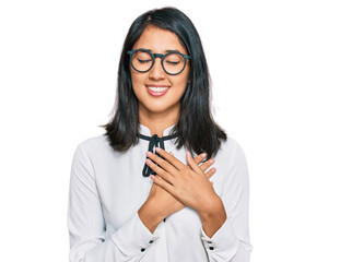 Beautiful asian young woman wearing business shirt and glasses smiling with hands on chest with closed eyes and grateful gesture on face. health concept.