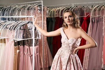 Young beautiful blonde girl wearing a full-length draped one shoulder pale pink satin slit prom...