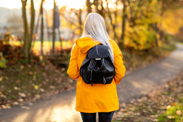 Weißhaarige Grauhaarige Frau spaziert im Park Herbst Sonnenstrahlen gelbe Regenmantel 