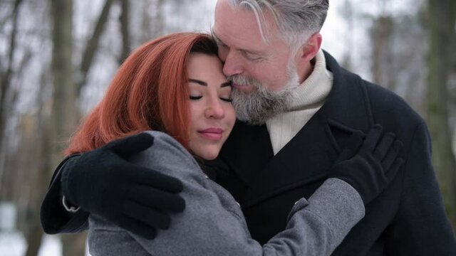 the image of tenderness and love of an adult couple of man and woman. Multi-aged husband and wife hug and bask while walking in a winter park, close-up