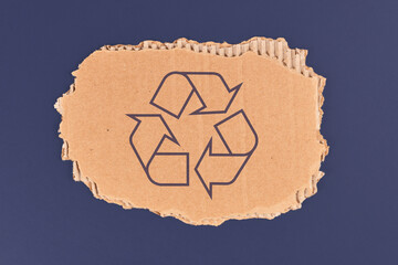 Piece of cardboard with recycling arrow sign on dark blue background