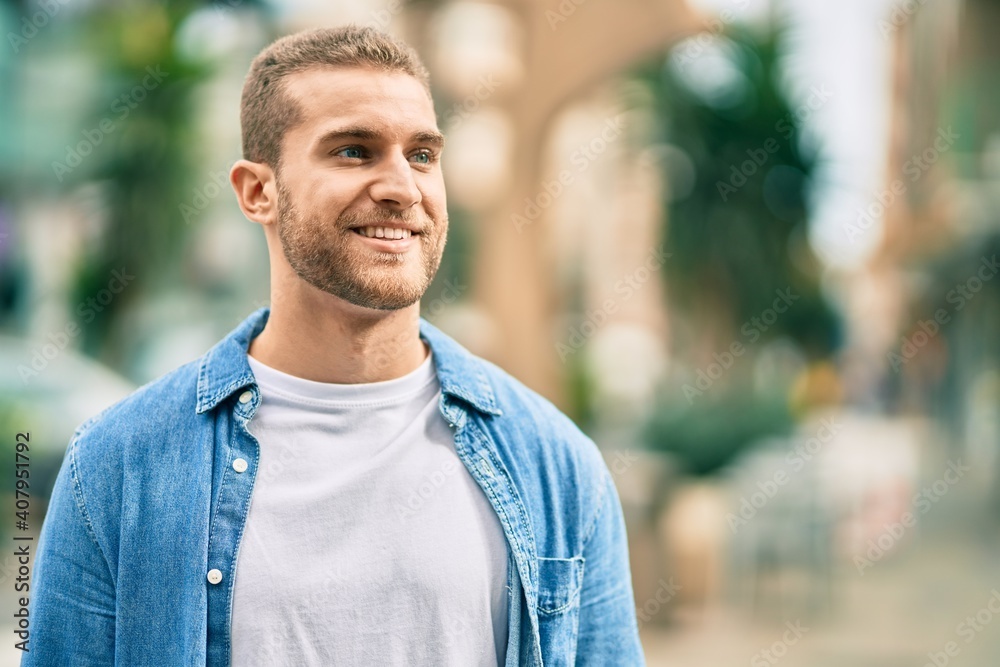 Wall mural Young caucasian man smiling happy standing at the city.