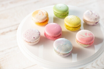 Multi-colored macaroons illuminated by sun rays casting their shadow, on light wood background, selective focus
