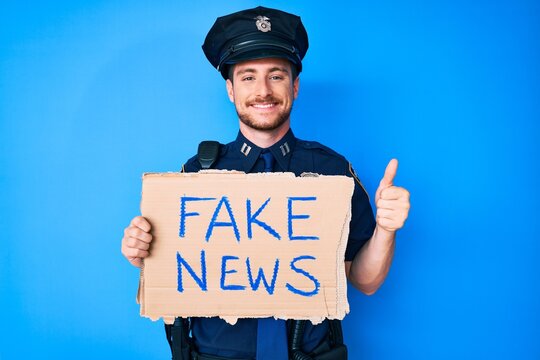 Young caucasian man wearing police uniform holding fake news banner smiling happy and positive, thumb up doing excellent and approval sign