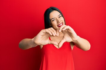 Young hispanic girl wearing casual style with sleeveless shirt smiling in love doing heart symbol shape with hands. romantic concept.