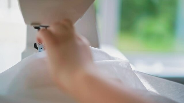 close up hands: woman during quarantine is engaged in remote work, sews to order, adjusts sewing machine and transporter with needle, puts transparent fabric