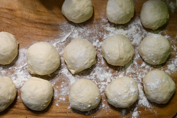 Top view of raw dough balls and flour on wooden counter. Preparation for cooking pastries.