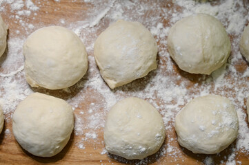 Top view of raw dough balls and flour on wooden counter. Preparation for cooking pastries.