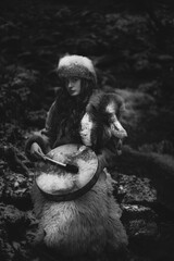Portrait of a woman wearing fur hat and fox fur pelt on her shoulders.Playing shamanic drum.Shot in forest surroundings.