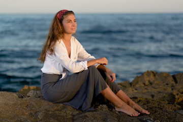 Fototapeta na wymiar Young pretty caucasian woman in white shirt and gray skirt having fun on the rocks by the sea shore