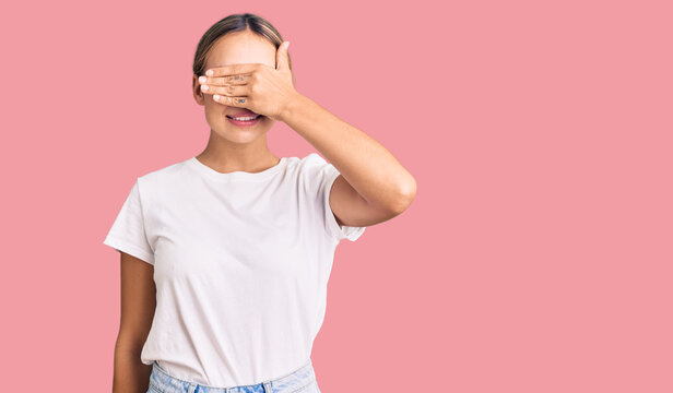 Young beautiful blonde woman wearing casual white tshirt smiling and laughing with hand on face covering eyes for surprise. blind concept.